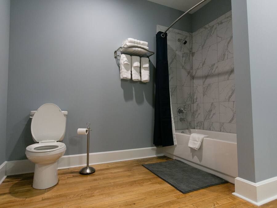 A bathroom with a toilet, a shower with a dark curtain, a bathtub, and a towel rack with folded towels.