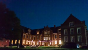 A large, historic building with multiple windows and a central entrance, surrounded by a well-maintained lawn and decorative lights.