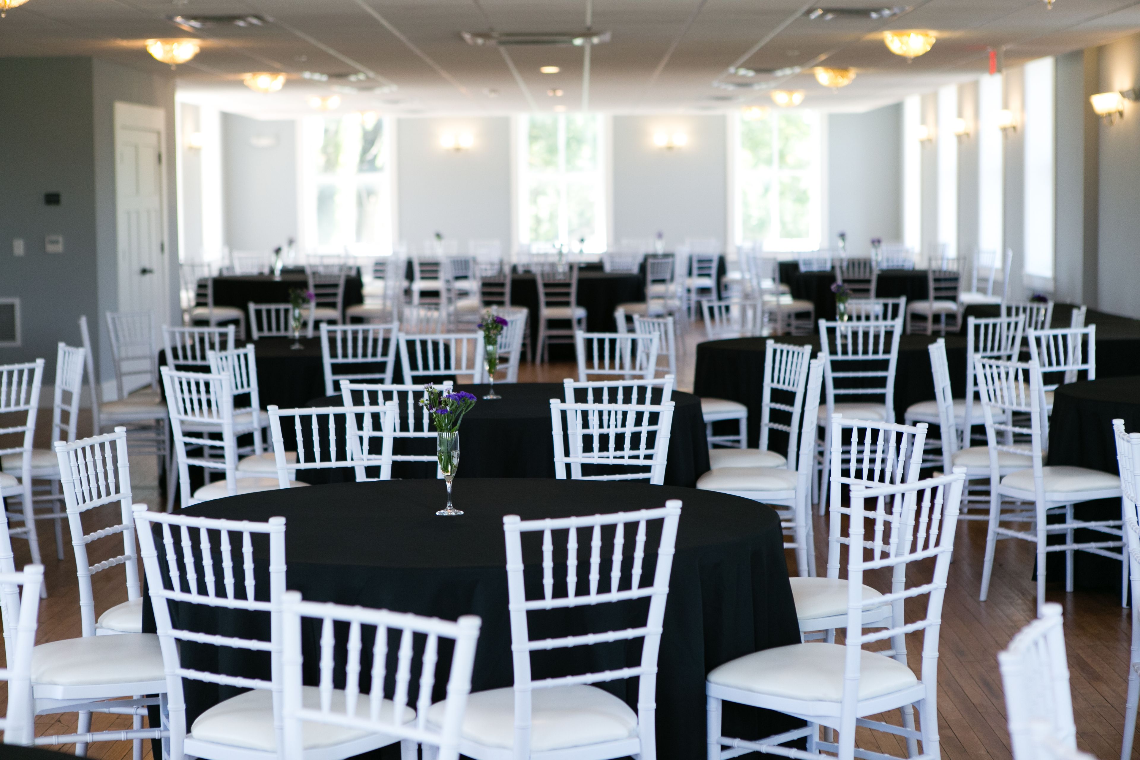 A banquet hall with round tables, white chairs, and black tablecloths.