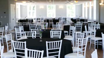 A banquet hall with round tables, white chairs, and black tablecloths.