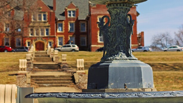 A multi-tiered fountain in a park with a red building in the background.