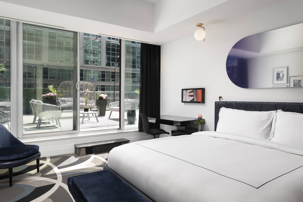 A modern hotel room with a large bed, a desk, and a view of the outdoors.