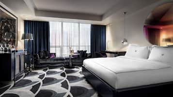 A modern hotel room with a large bed, a desk, a sofa, and a minibar.