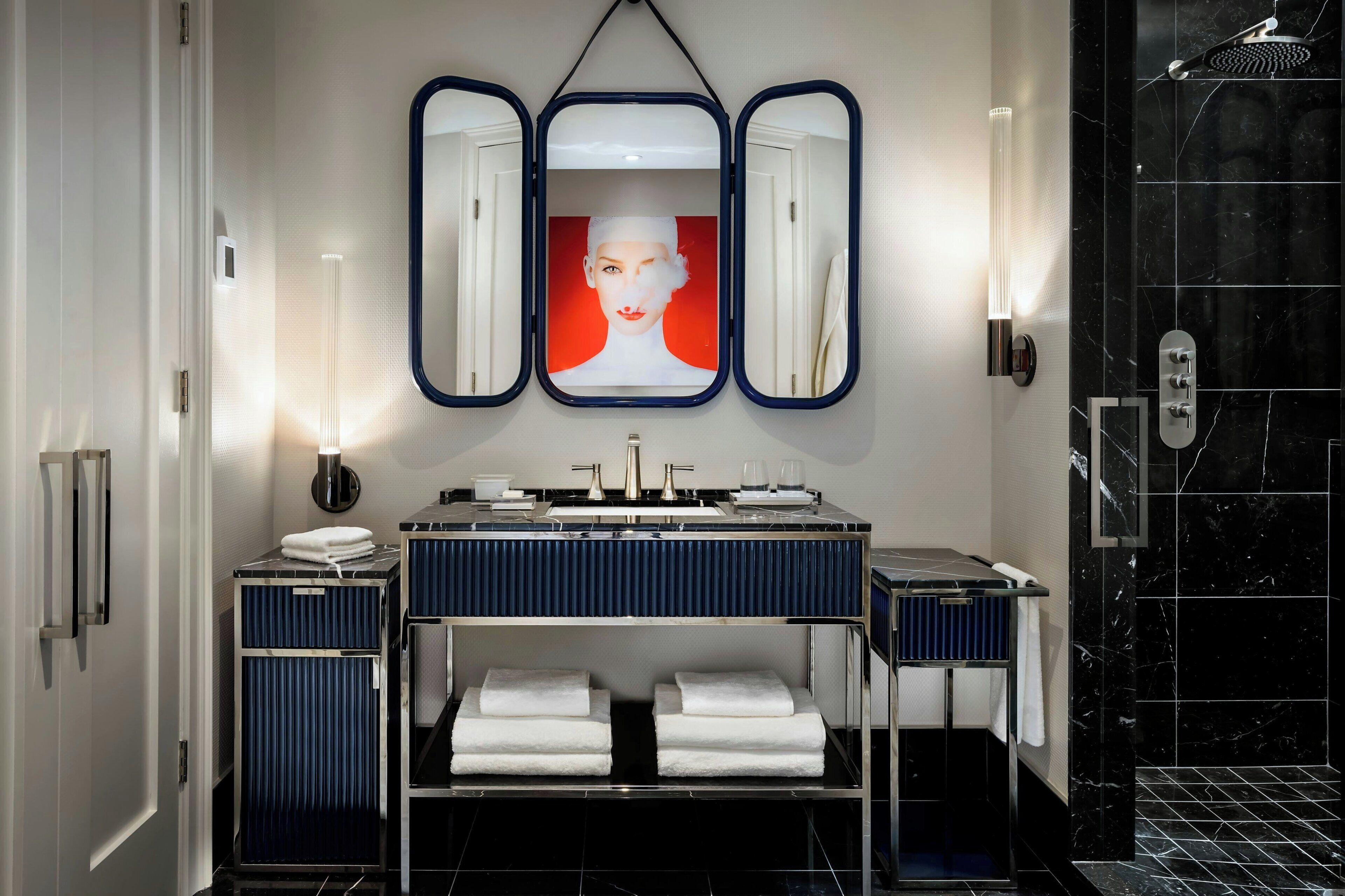 A modern bathroom with a vanity, a triple mirror, and a shower area.