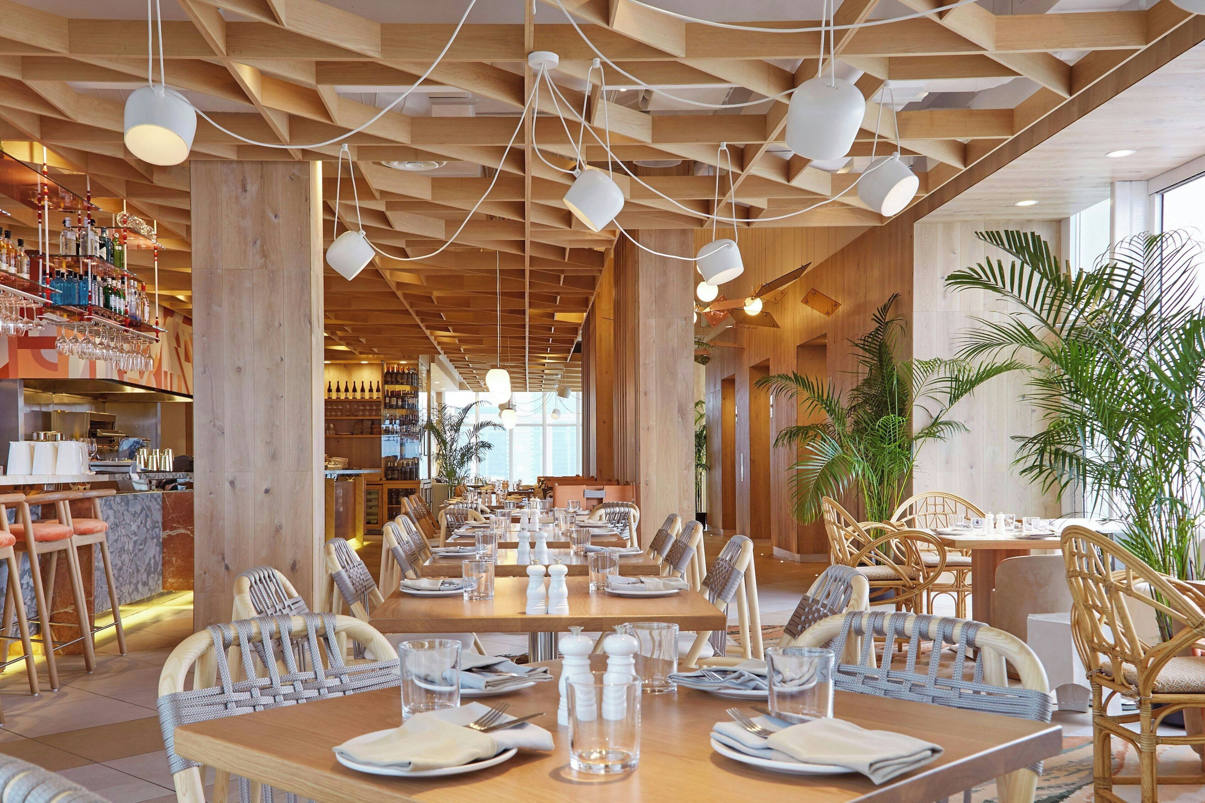 Ein Restaurantinneres mit Holzbalkendecke, hängenden Pendelleuchten und einer Bar mit Regalen voller Flaschen.