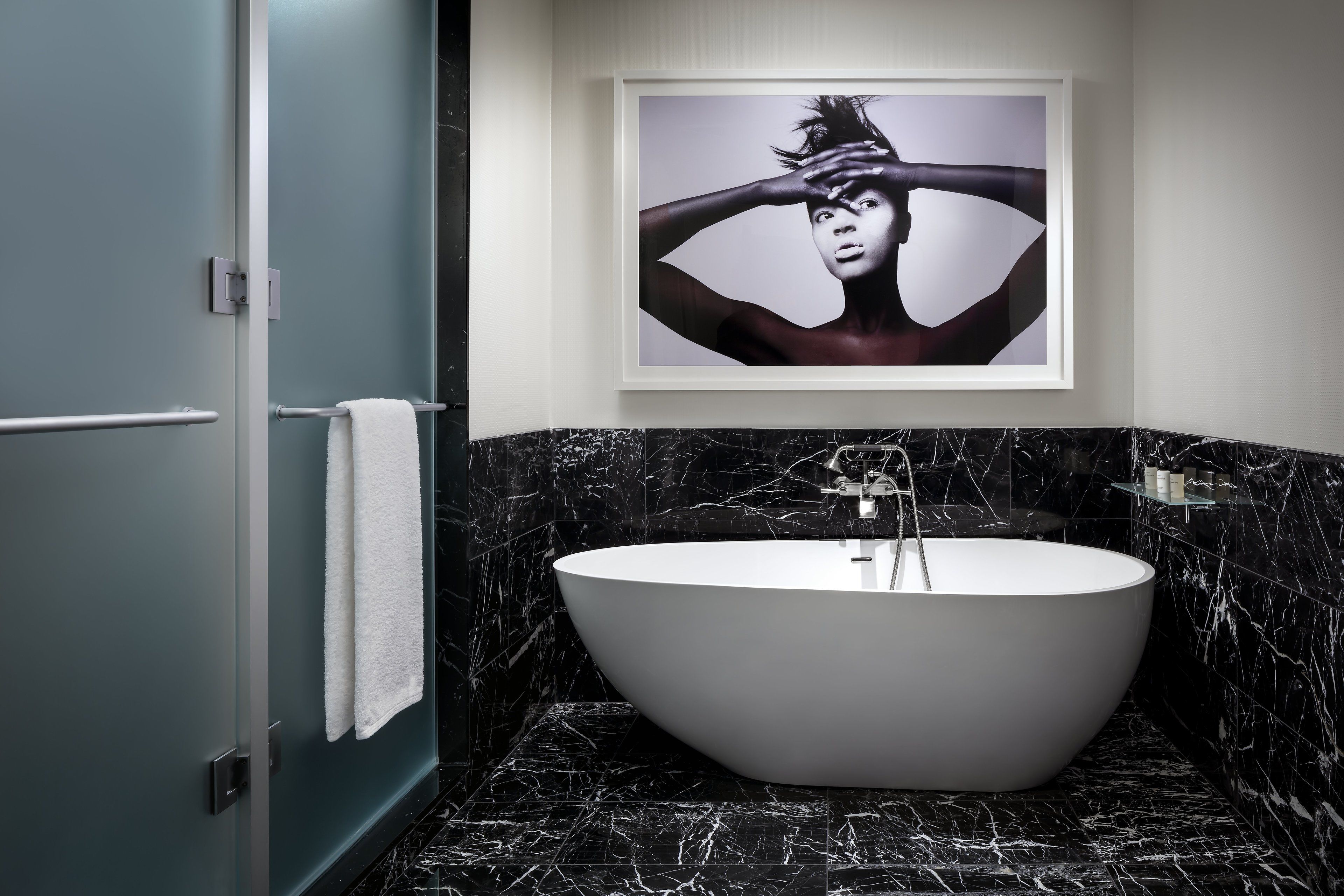A modern bathroom with a freestanding bathtub, marble walls, and a framed artwork above the tub.