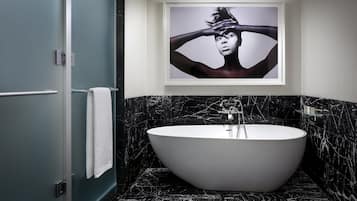 A modern bathroom with a freestanding bathtub, marble walls, and a framed artwork above the tub.