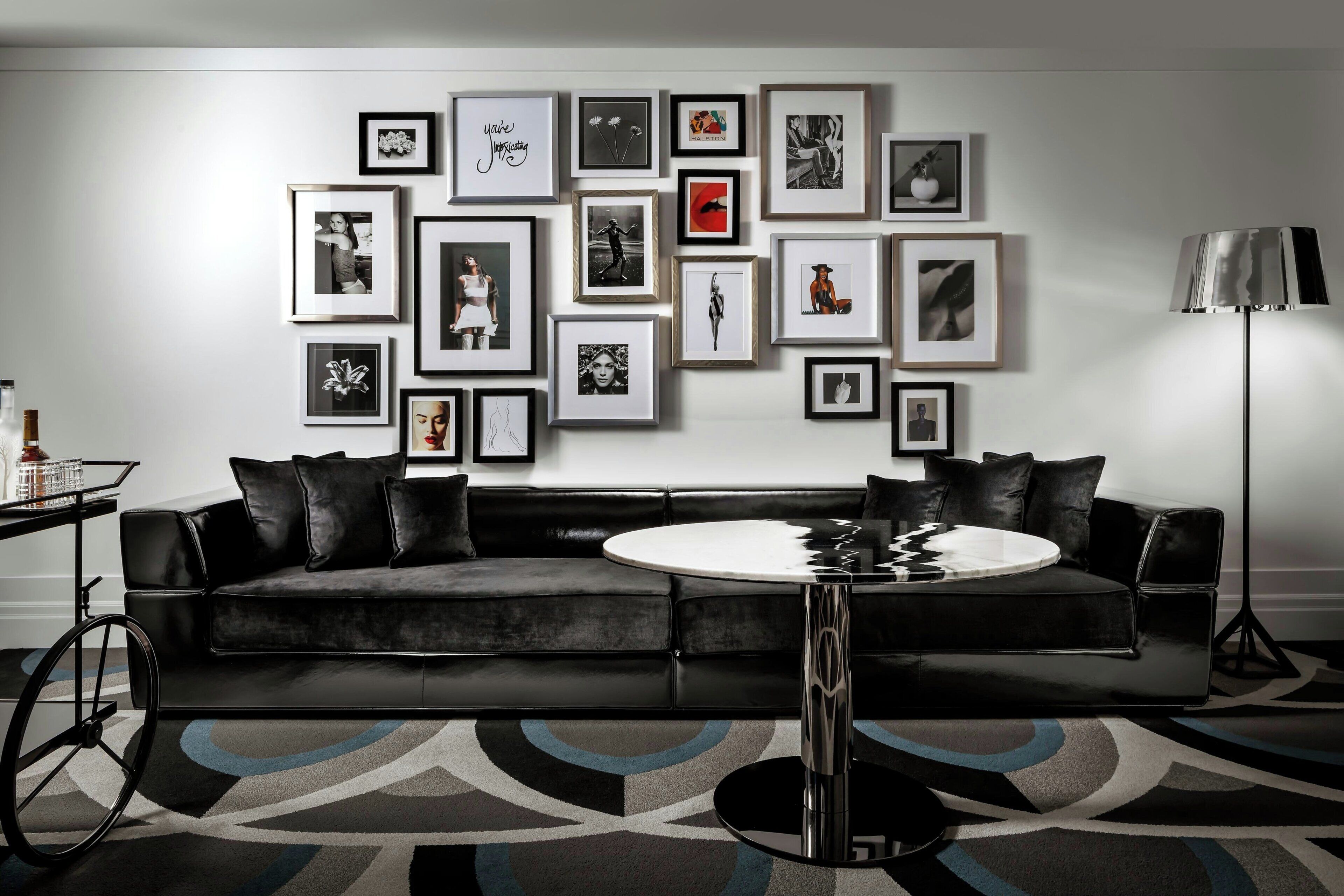 Una sala moderna con un sofá de cuero negro, una mesa redonda de centro y una pared decorada con varias fotos enmarcadas.