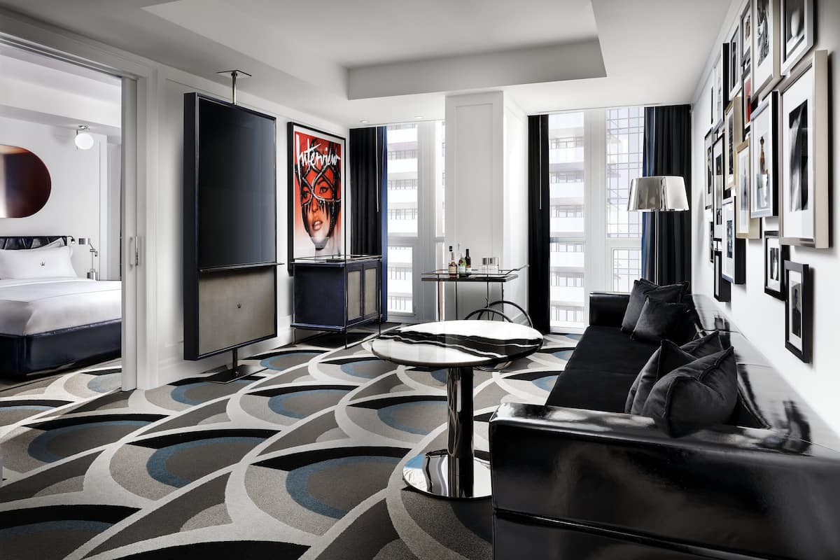 A modern hotel room with a large bed, a sofa, a TV, and a dining area.