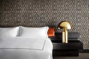 Een net opgemaakt bed met witte lakens en een gouden lamp op een zwart nachtkastje.