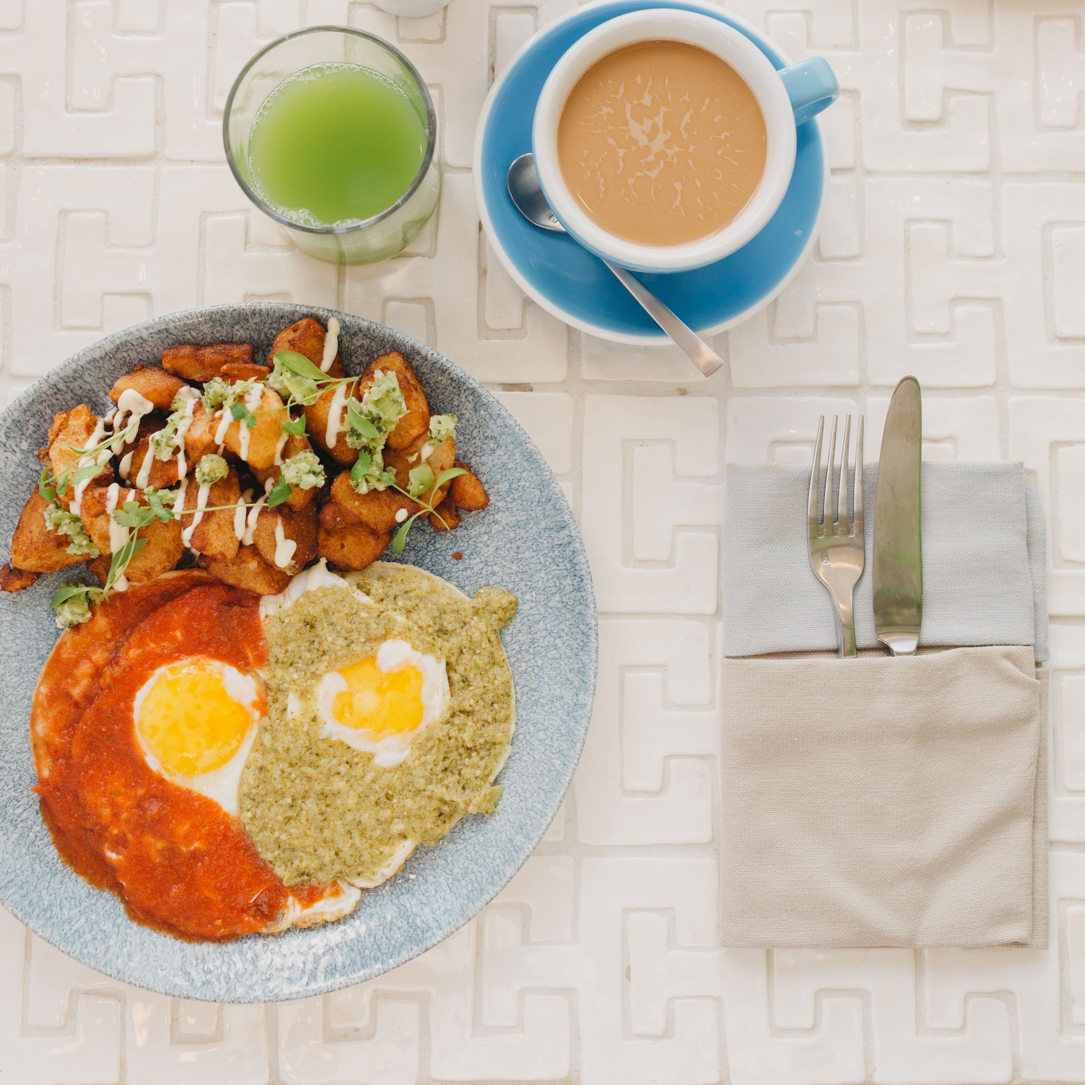 Un plato de comida con salsa verde, un alimento frito con salsa y un huevo frito sobre un mantel estampado.