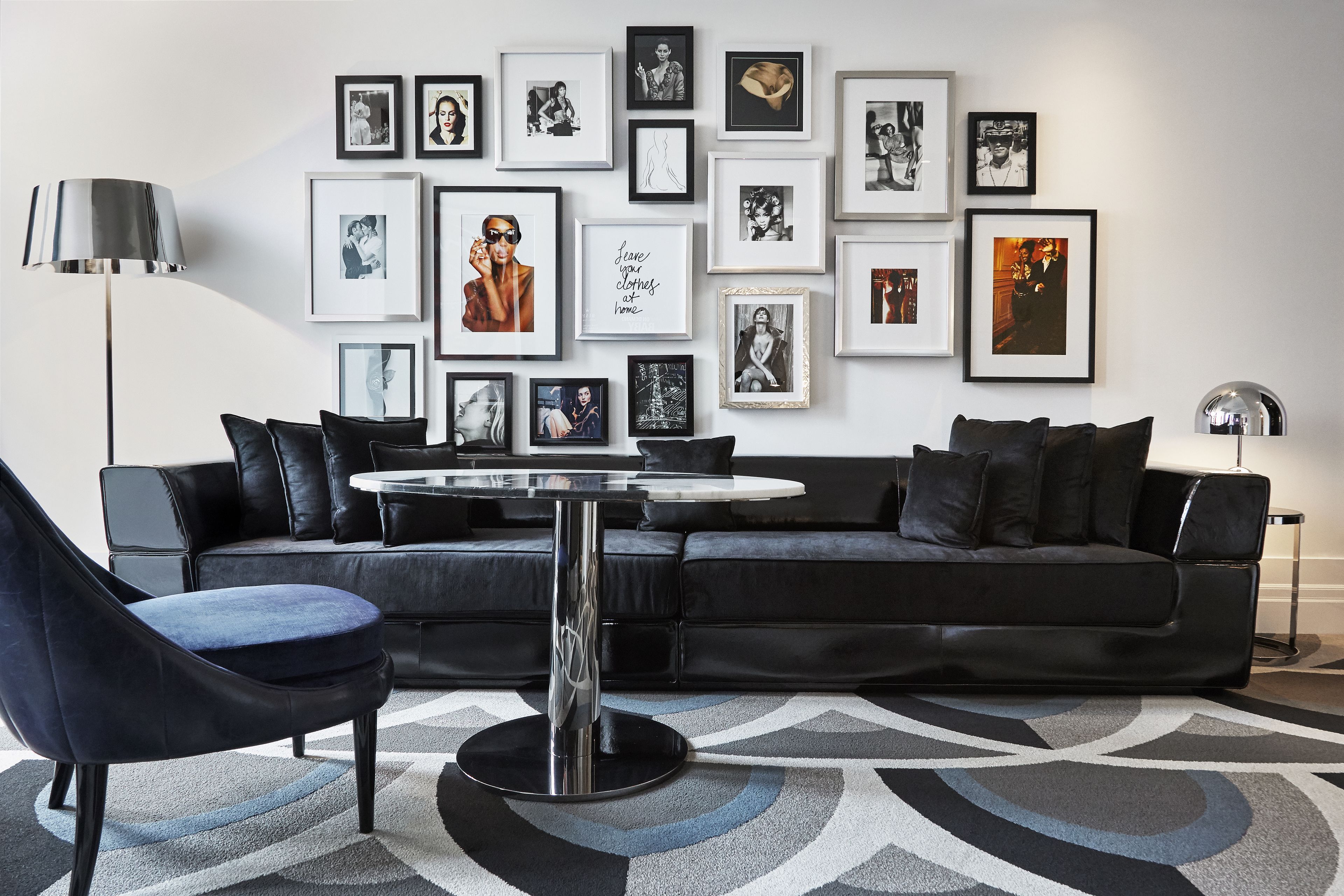 Een moderne woonkamer met een zwarte leren bank, een ronde salontafel en een kamerbreed tapijt met een patroon.