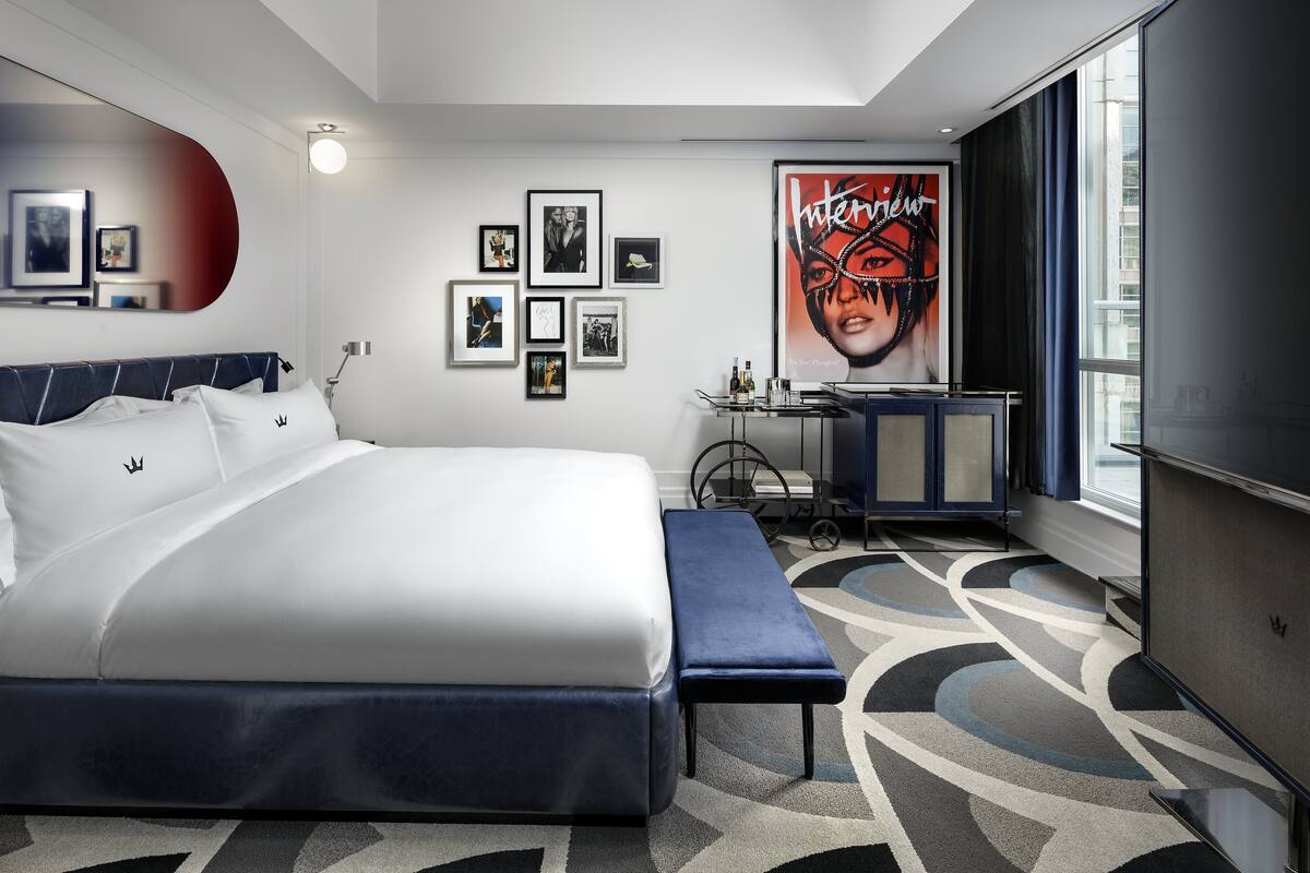 A modern hotel room with a large bed, a desk, and a large window.