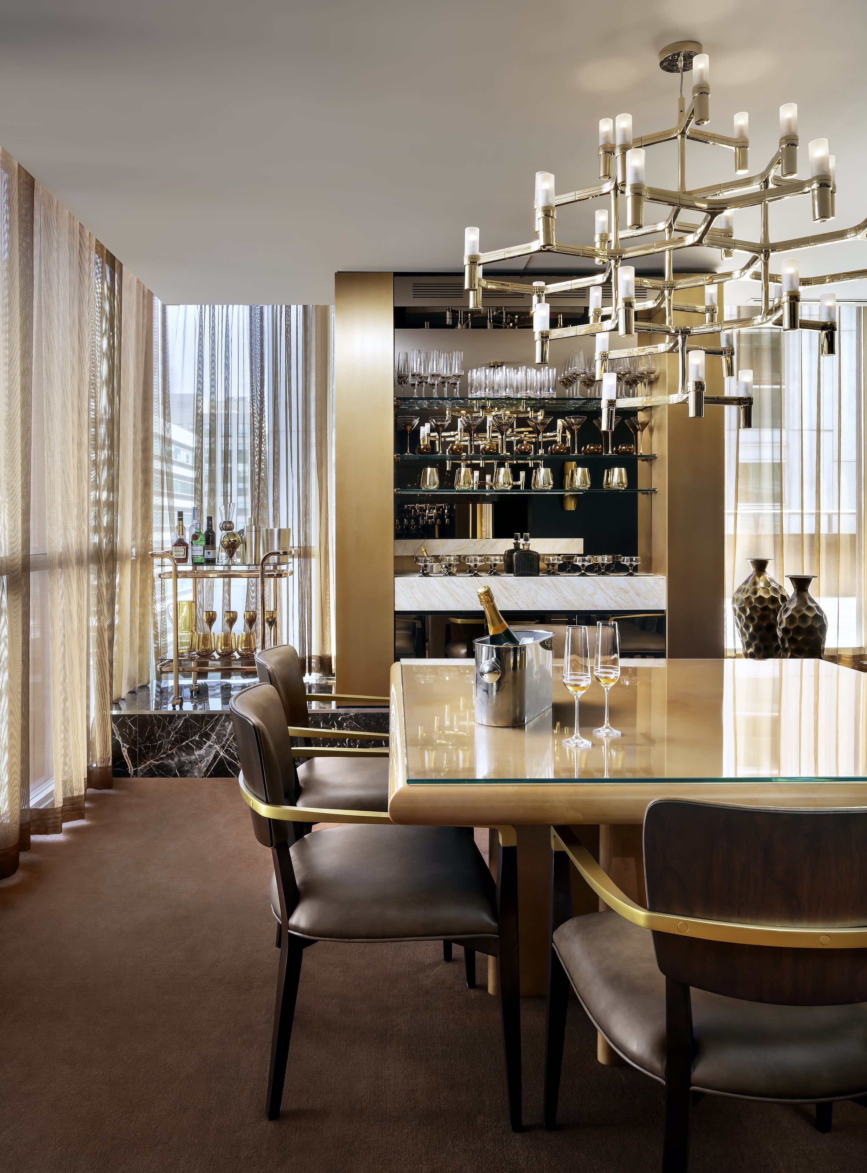 A modern bar area with a glass table, multiple chairs, and a chandelier.