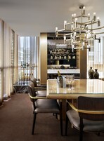 A modern bar area with a glass table, multiple chairs, and a chandelier.