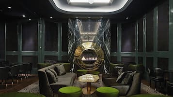 A modern lounge area with a central fireplace, comfortable seating, and a patterned floor.