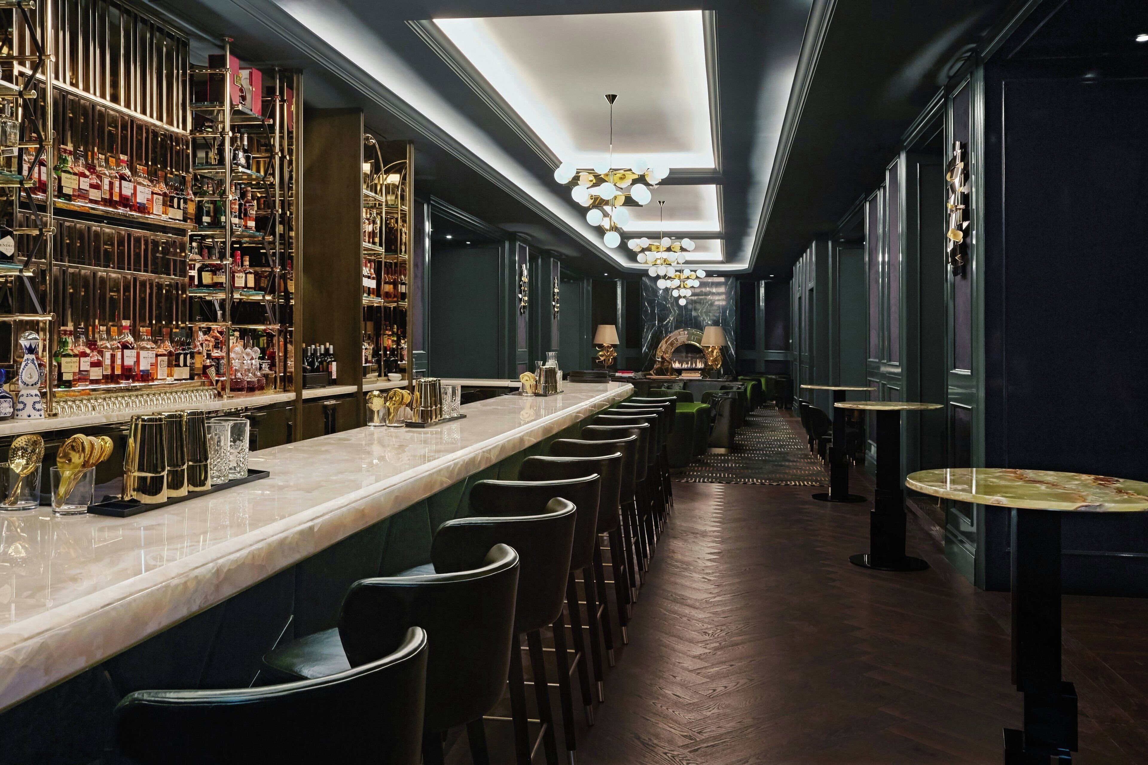 Una zona de bar con una barra larga, varios taburetes y una gran variedad de botellas y copas.