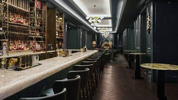 Una zona de bar con una barra larga, varios taburetes y una gran variedad de botellas y copas.