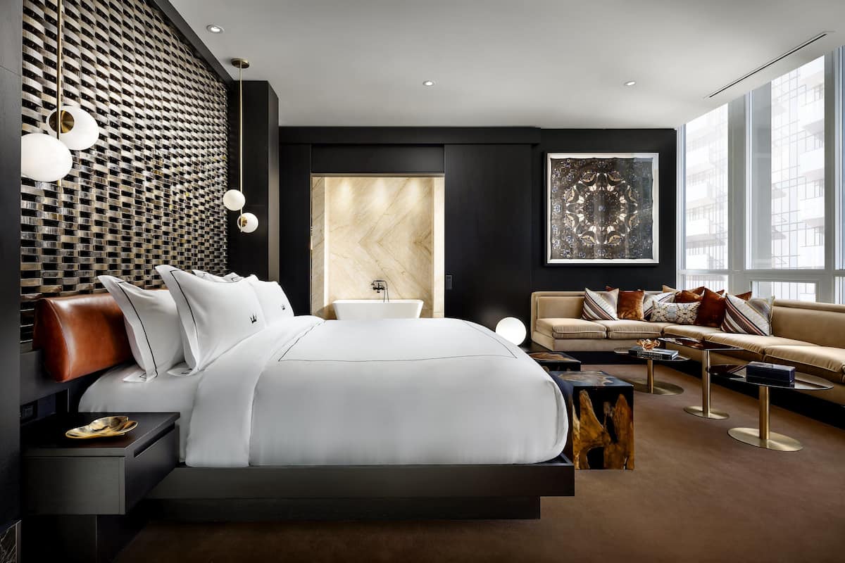 A modern bedroom with a large bed, a sofa, a dining table, and a decorative wall.