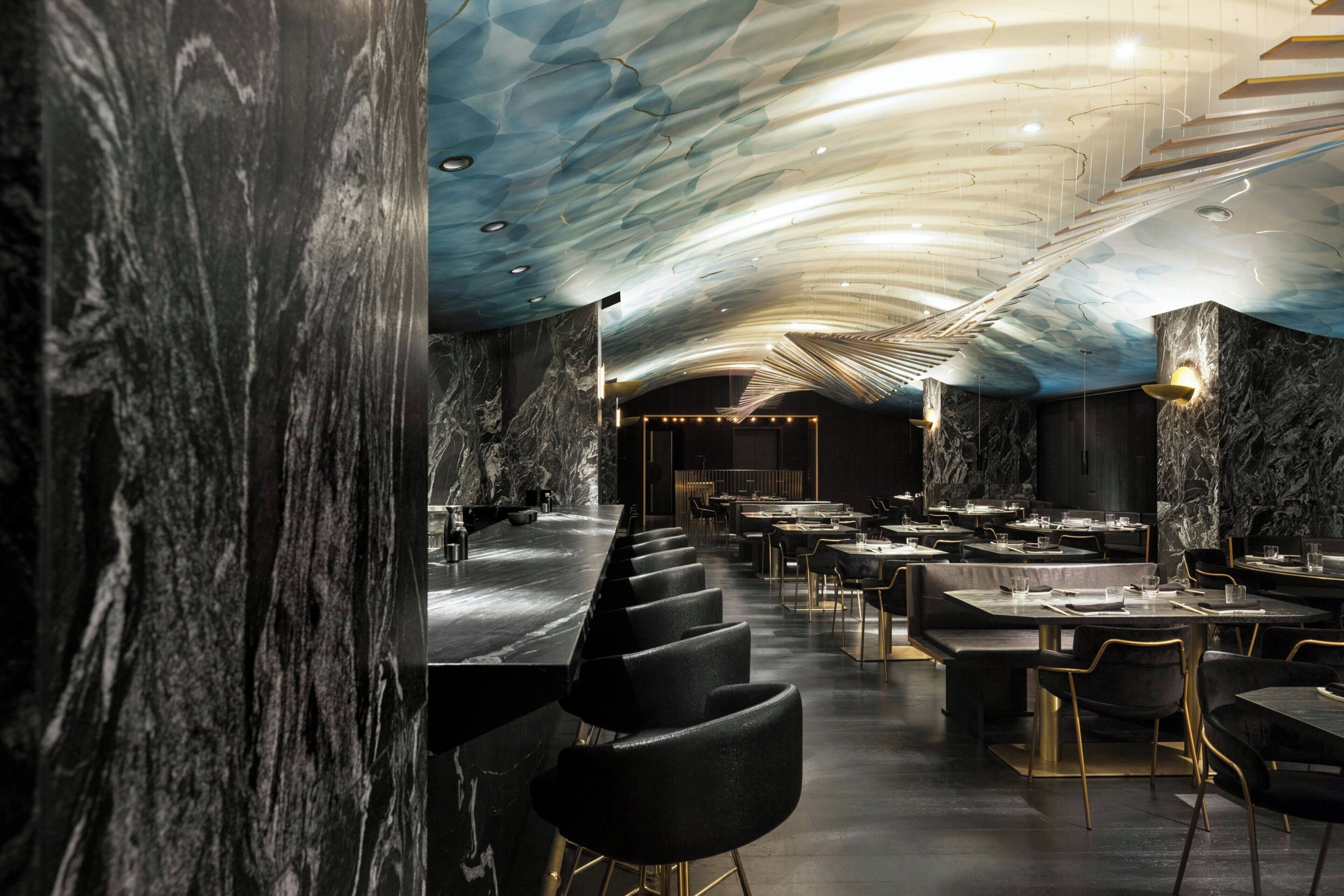 Un intérieur de restaurant moderne avec des murs en marbre, un long comptoir et de nombreuses tables et chaises.