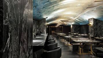 Un intérieur de restaurant moderne avec des murs en marbre, un long comptoir et de nombreuses tables et chaises.