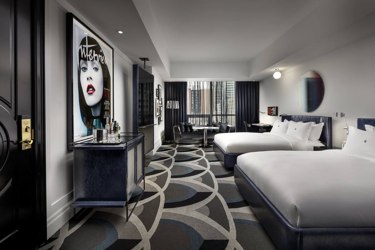 A hotel room with two beds, a desk, a chair, a TV, and a large window with curtains.