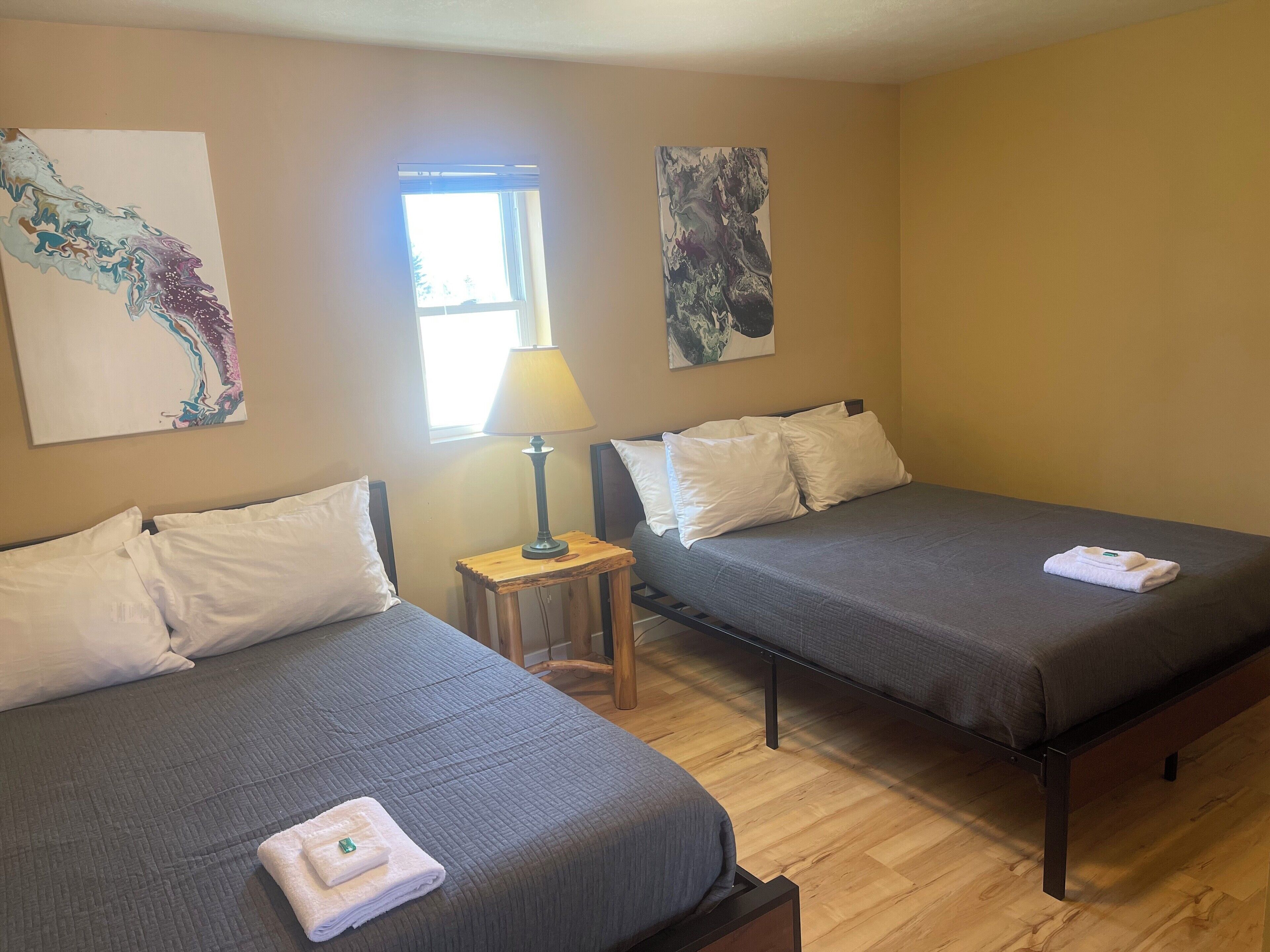 Une chambre d’hôtel avec deux lits, une petite table avec une lampe et des œuvres d’art accrochées aux murs.