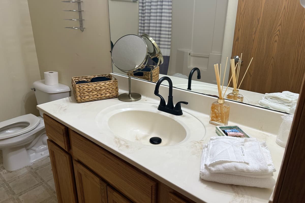 A bathroom with a white sink, black faucet, and a mirror above it. There is a toilet visible to the left and a wooden cabinet below the sink.