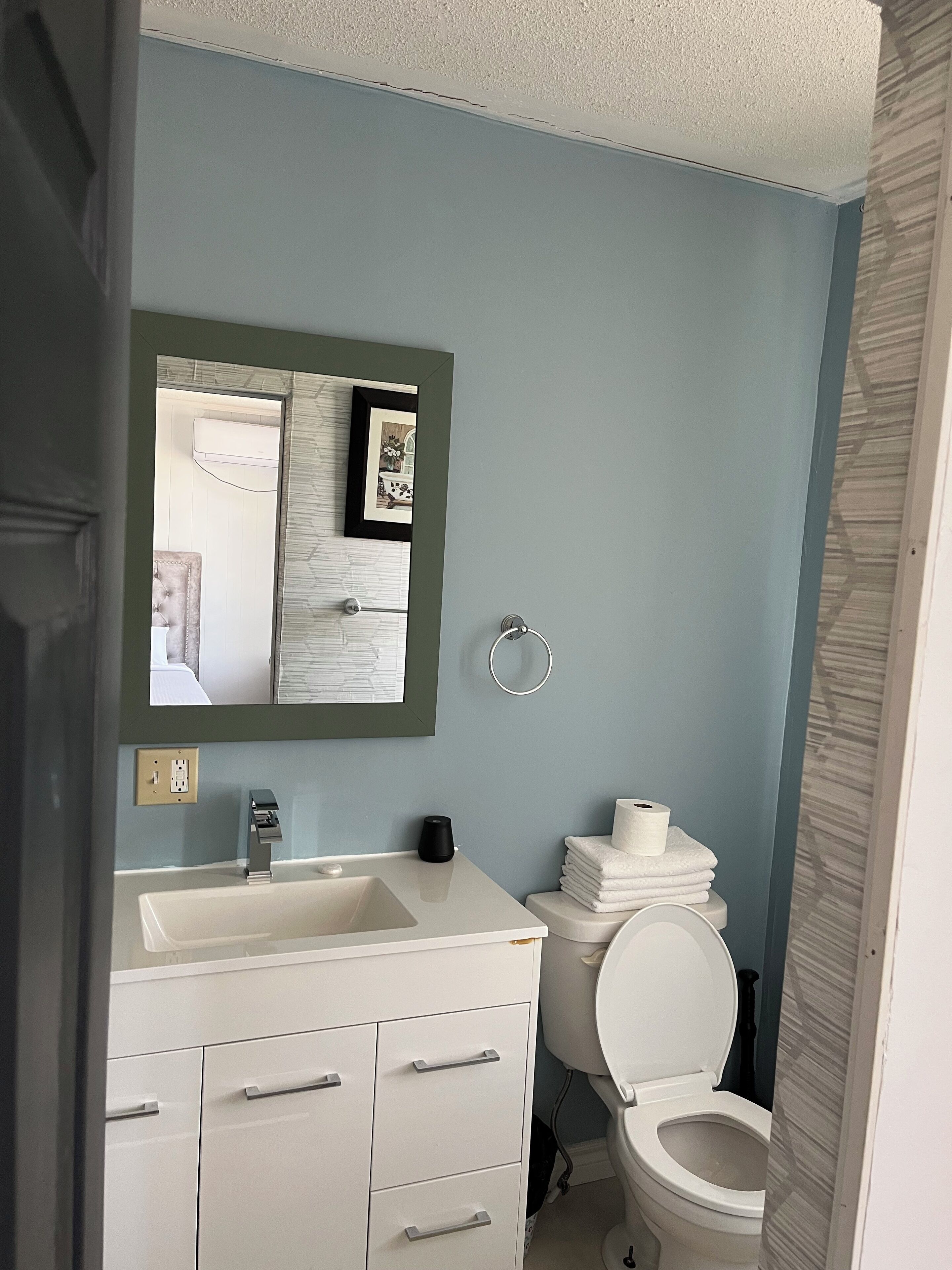 A bathroom with a white sink, a mirror, a toilet, and a towel stack.