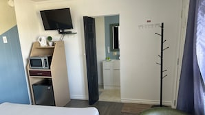 Ein Hotelzimmer mit Bett, Schreibtisch mit Computer, Mikrowelle, Kühlschrank, Wand-Fernseher und einem durchgehenden Türbogen einsehbarer Badezimmer.