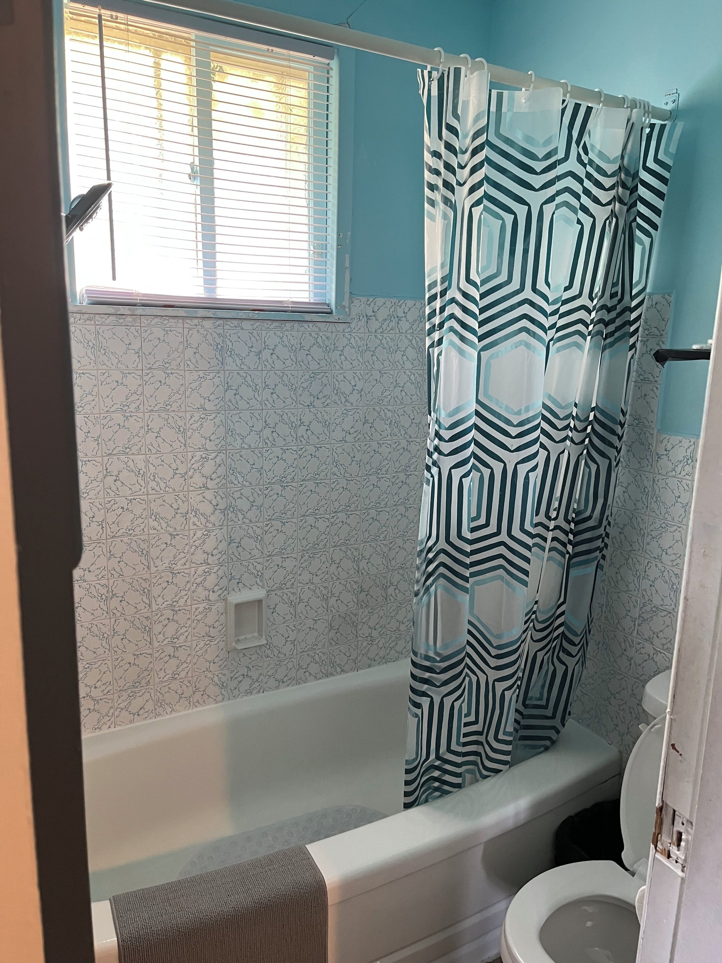 A bathroom with a bathtub, toilet, and a window with blinds.
