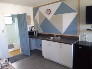Compact kitchen with modern design, featuring a microwave, sink, and refrigerator, complemented by a geometric patterned wall and a clock.