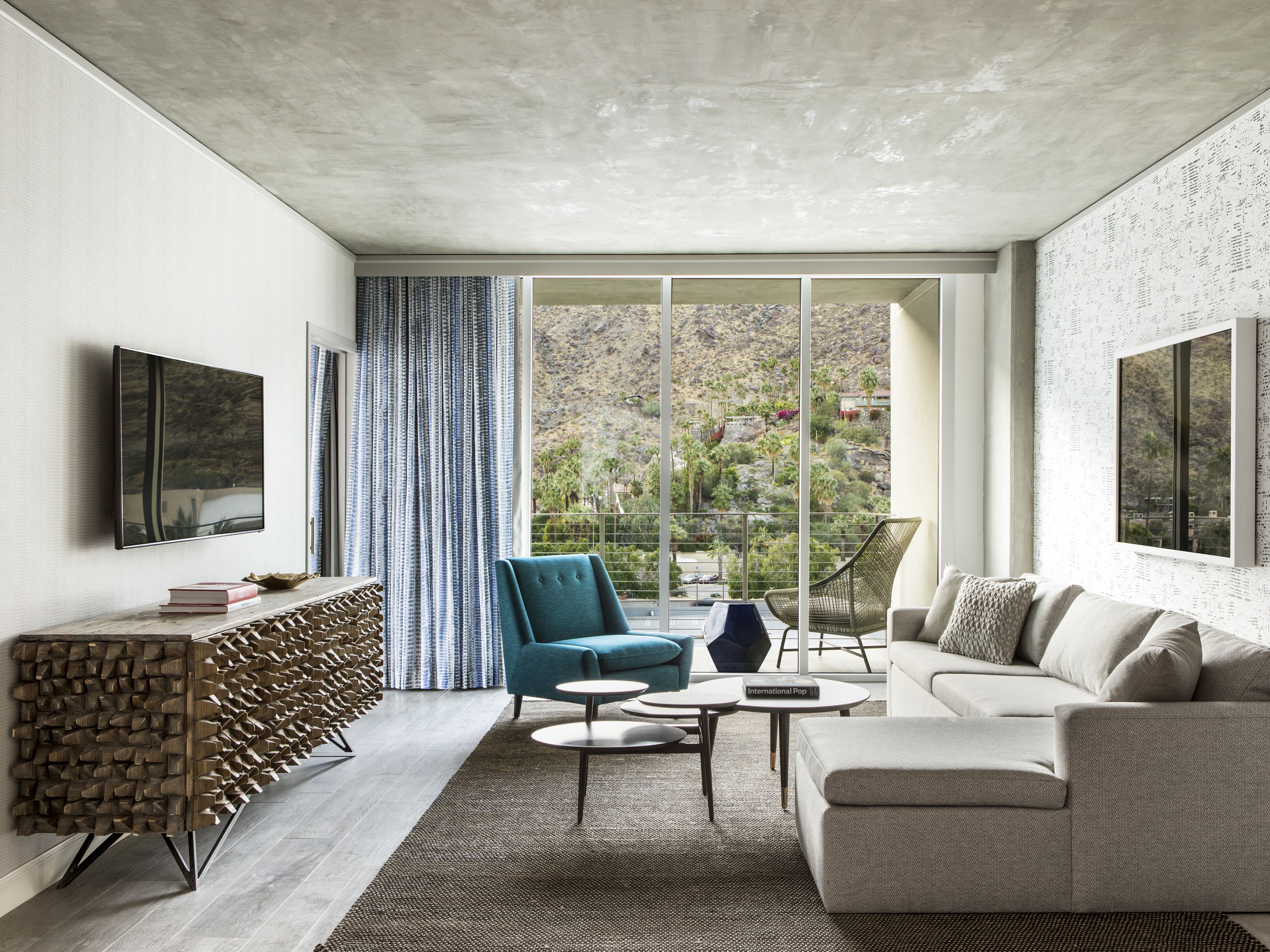 A modern living room with a sofa, a blue armchair, a coffee table, and a TV mounted on the wall.
