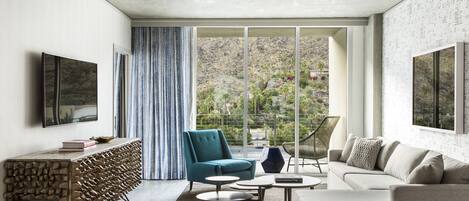 A modern living room with a sofa, a blue armchair, a coffee table, and a TV mounted on the wall.