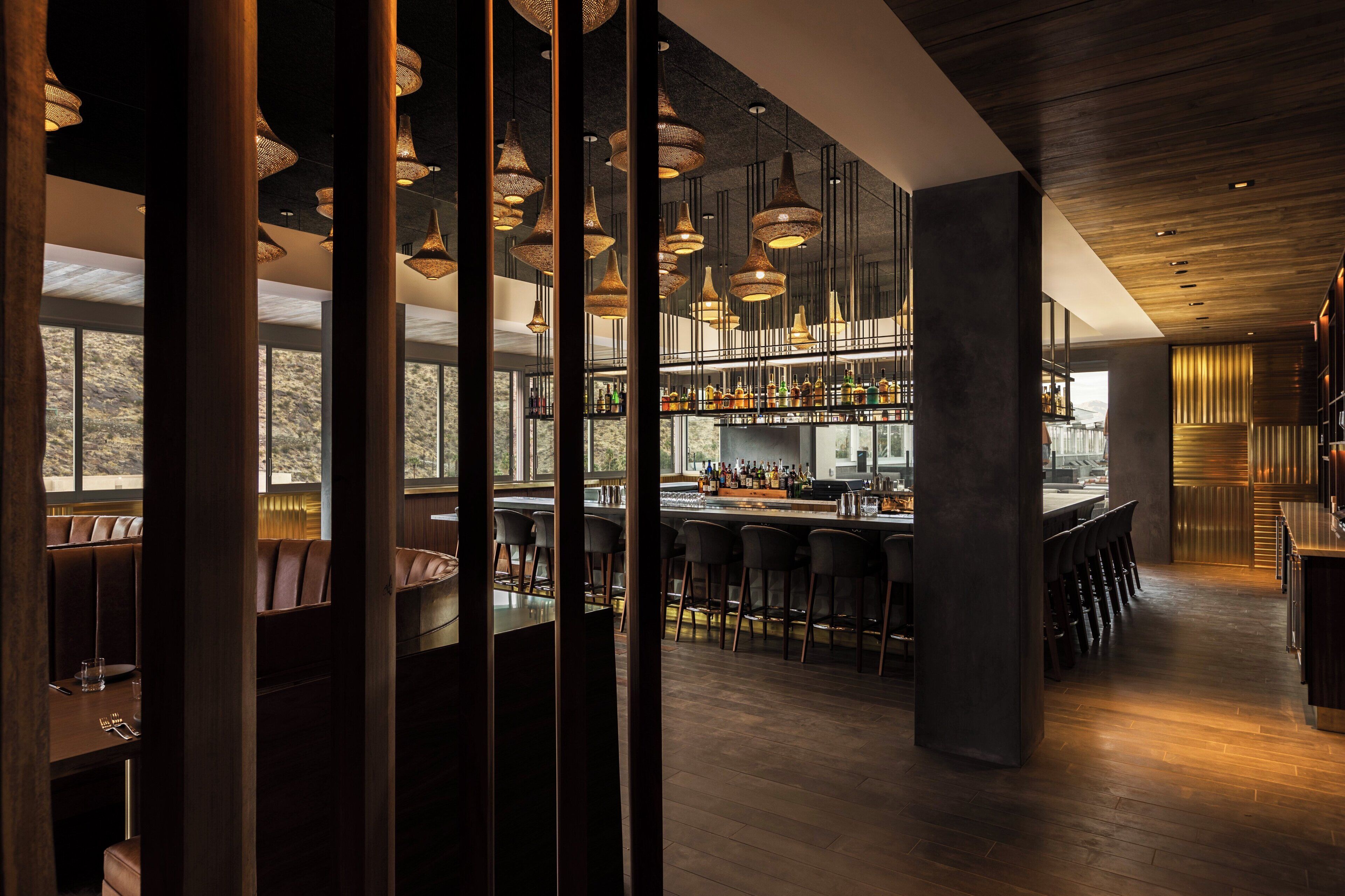 Zona de bar con varias opciones de asientos, incluyendo taburetes y cabinas, y una variedad de botellas y vasos en las estanterías.