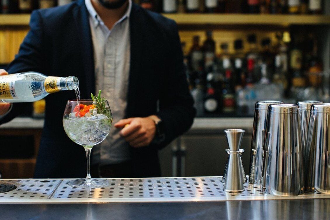 Un barman sirve una bebida en un vaso con hielo y una guarnición.