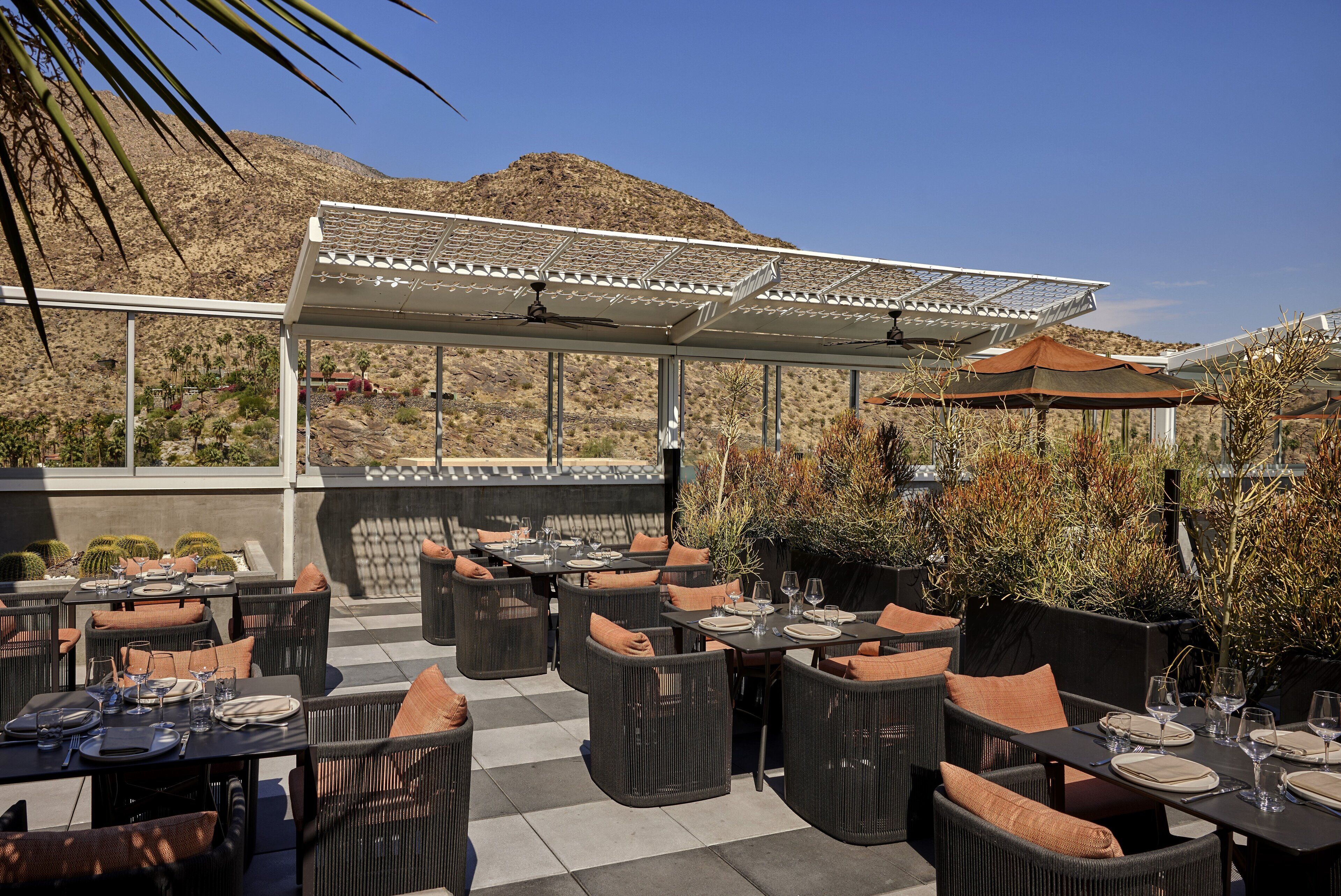 Een buitenterras met tafels en stoelen, een pergola en uitzicht op een berg.