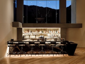 A modern bar area with a long counter, multiple stools, and a variety of bottles and glasses. - Kimpton Rowan Palm Springs Hotel by IHG (Palm Springs)