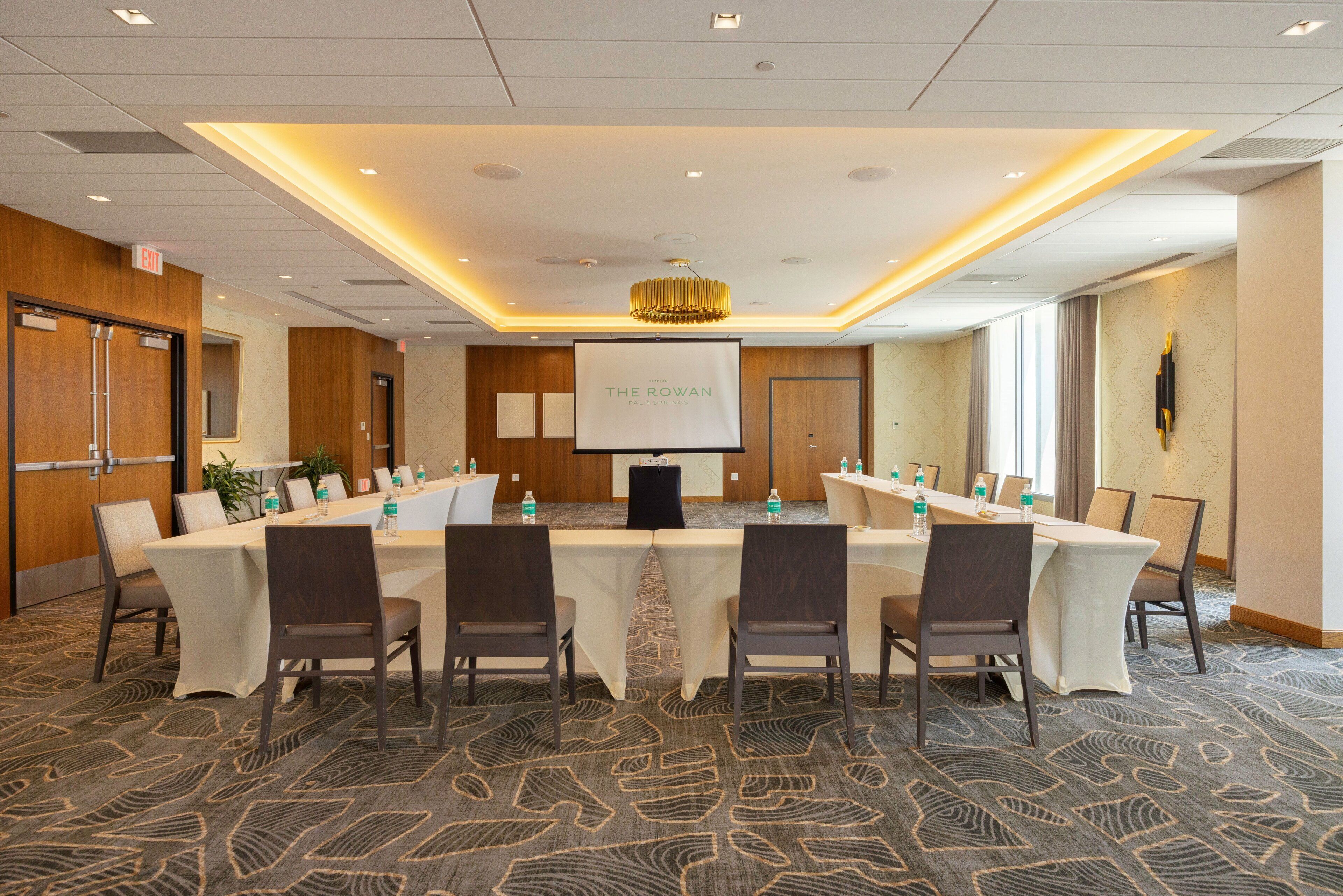 A conference room with a long table, chairs, a projector screen, and a carpeted floor.