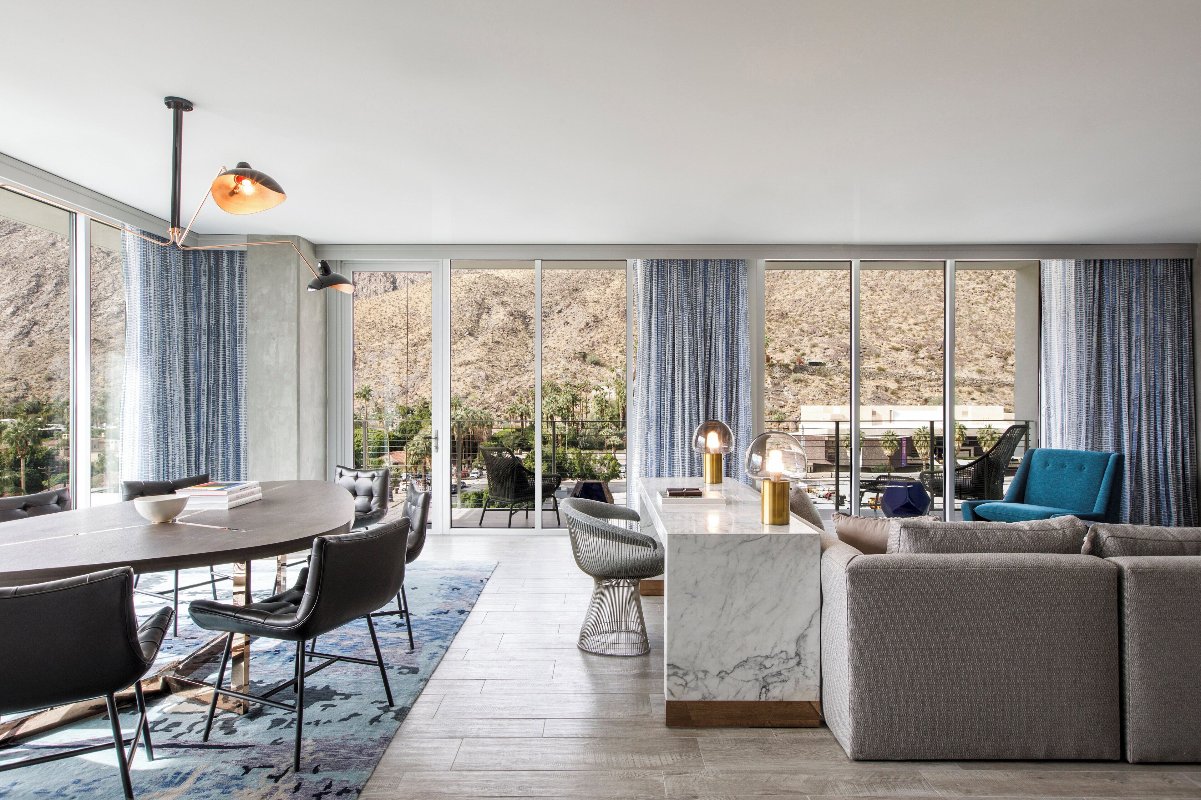 A modern living room with a dining area, large windows, and a view of a mountainous landscape.