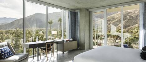 A modern hotel room with a large bed, a desk, and a view of mountains.