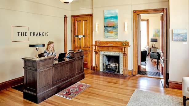 A reception area with a wooden desk, a fireplace, and a painting on the wall. - The Francis (Portland)