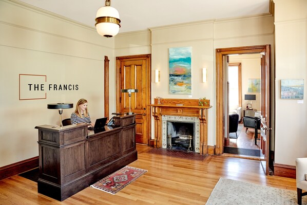 A reception area with a wooden desk, a fireplace, and a painting on the wall. - The Francis (Portland)