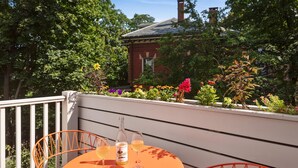 A balcony with a round table and orange chairs, overlooking a garden with various plants and flowers. - The Francis (Portland)