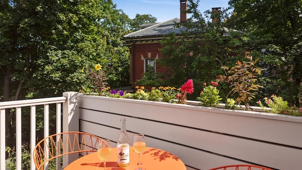 A balcony with a round table and orange chairs, overlooking a garden with various plants and flowers. - The Francis (Portland)
