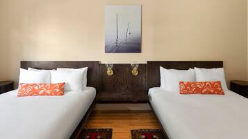A hotel room with two beds, each with white bedding and orange pillows, a wooden headboard, a wall-mounted artwork, and a patterned rug.