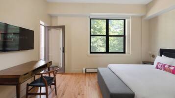 A bedroom with a bed, a desk, a chair, a TV, and a window with a view of trees.