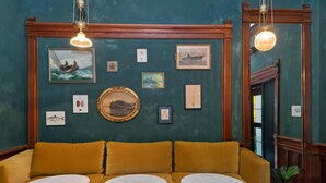 A room with a mustard-colored sofa, two round tables, and various framed artworks on the walls. - The Francis (Portland)