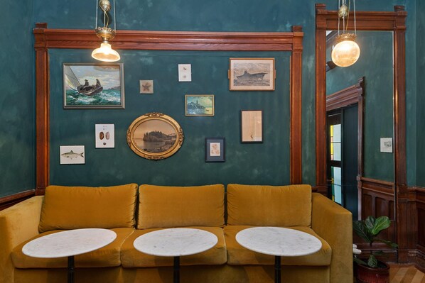 A room with a mustard-colored sofa, two round tables, and various framed artworks on the walls. - The Francis (Portland)