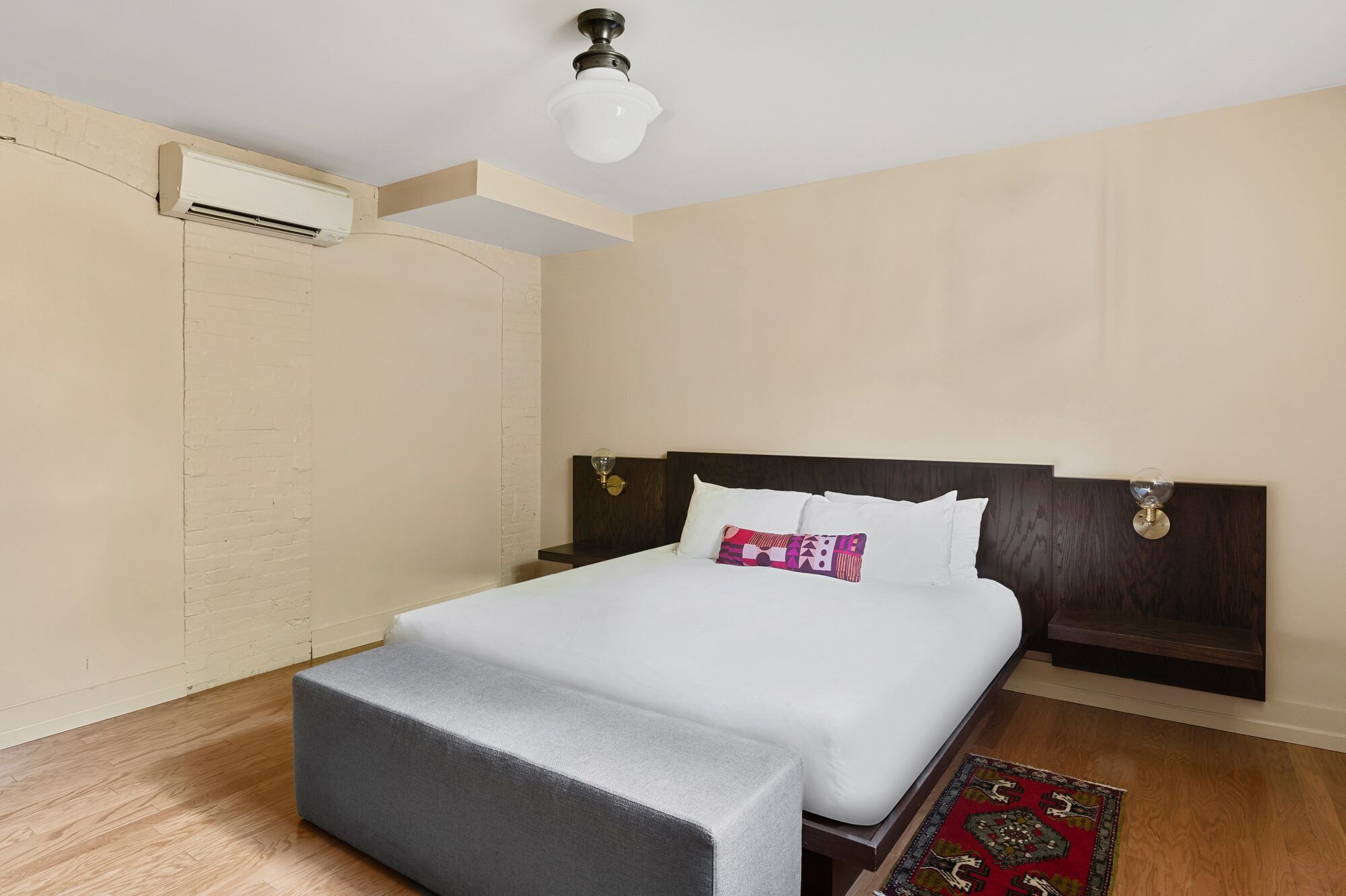 Una camera d'hotel con un letto, un comodino, un'unità di condizionamento a muro e una luce a soffitto.